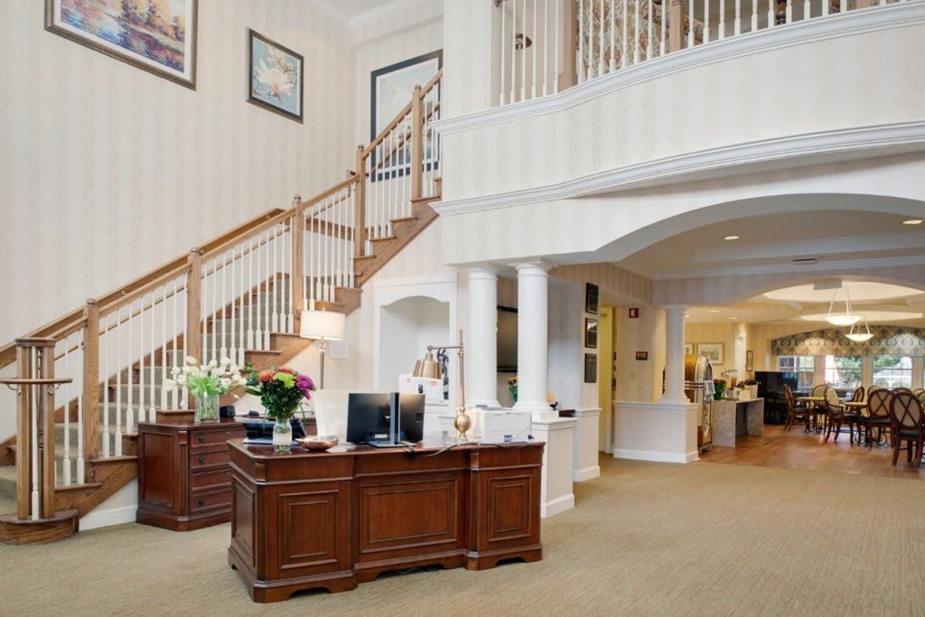 A well-decorated office reception area featuring wooden desks, a staircase, and elegant decor.