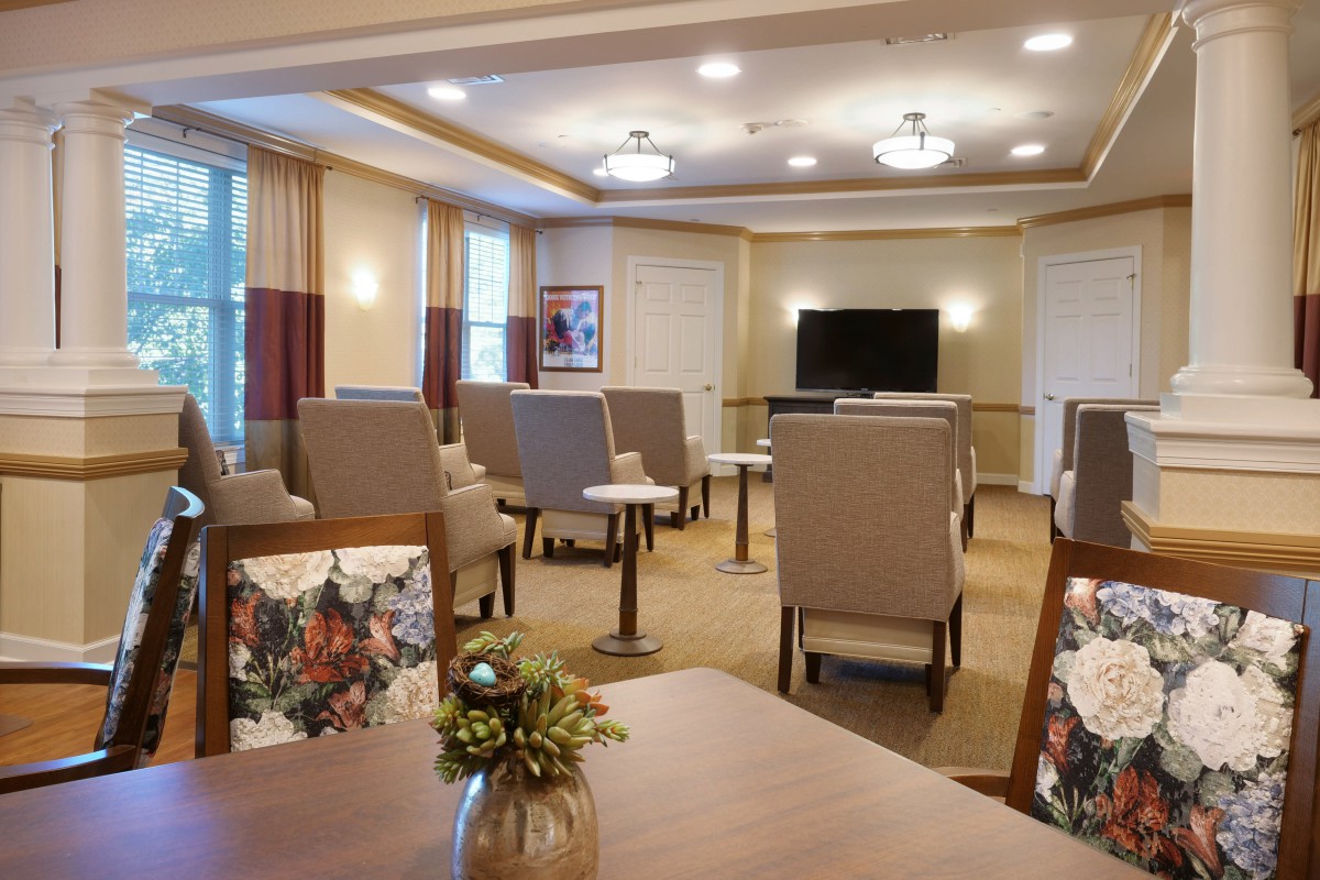 A well-lit community room with arranged seating, tables, and a television.