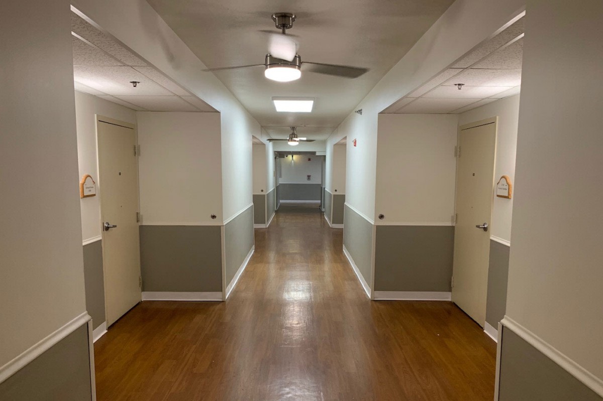 A long hallway with multiple doors, a ceiling fan, and wooden flooring.