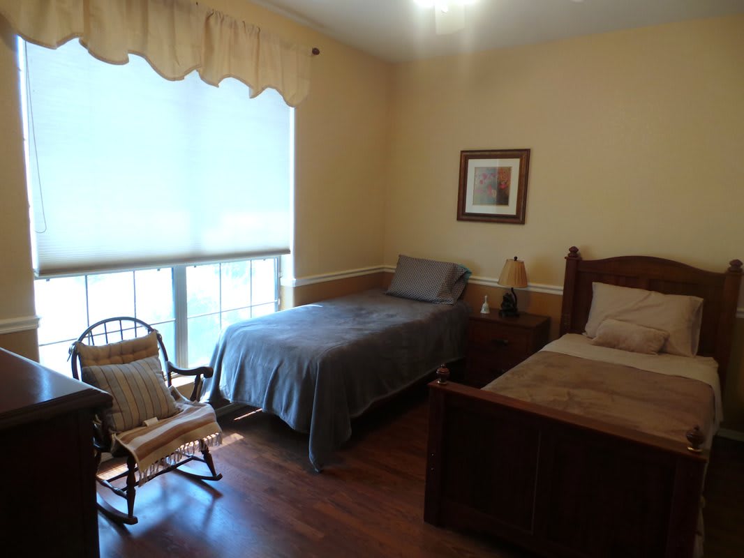 A cozy bedroom with two beds, a rocking chair, and a large window.