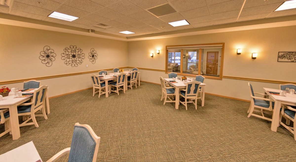 An empty dining room with several tables and chairs, featuring a carpeted floor and decorative lighting.