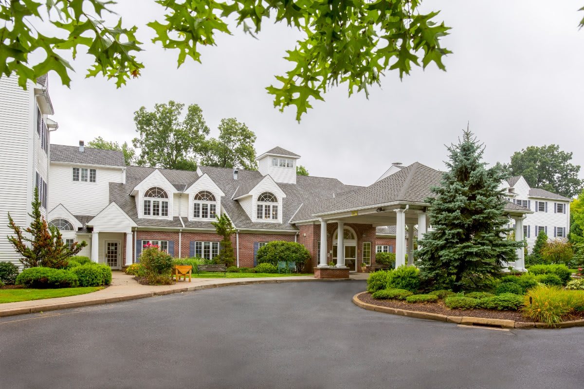 A large residential building with a landscaped entrance and driveway, surrounded by trees.