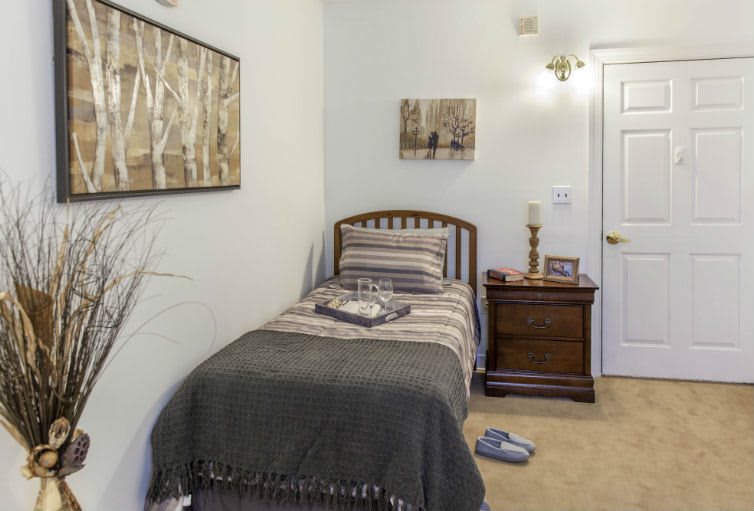 A cozy bedroom featuring a single bed with striped bedding, complemented by minimalist artwork and a wooden nightstand.