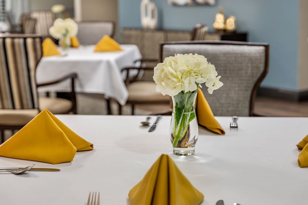 A beautifully set dining table with yellow napkins and a vase of white flowers.