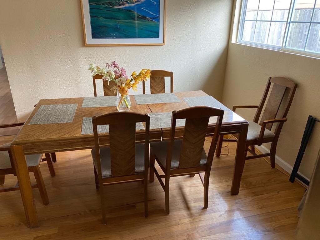 A cozy dining room with a wooden table and chairs, adorned with a vase of flowers, under natural daylight.