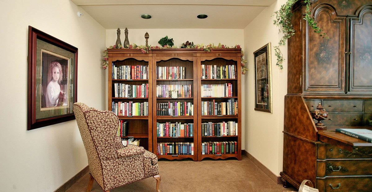 A cozy reading nook featuring a large wooden bookshelf filled with books and a comfortable patterned chair.