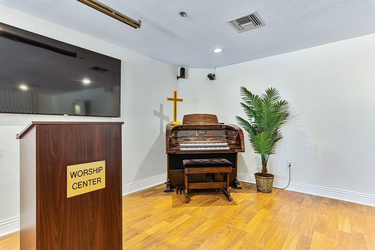 A small worship center with a piano, podium, and cross.