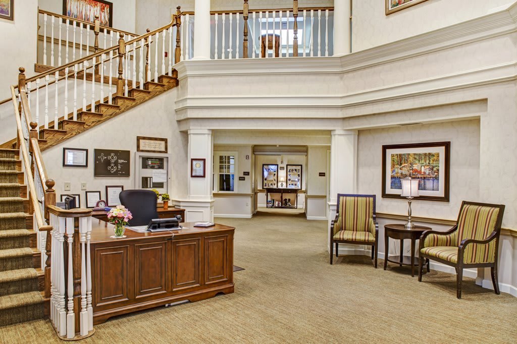 A spacious and elegantly designed office reception area featuring a wooden desk, chairs, artwork, and a staircase.