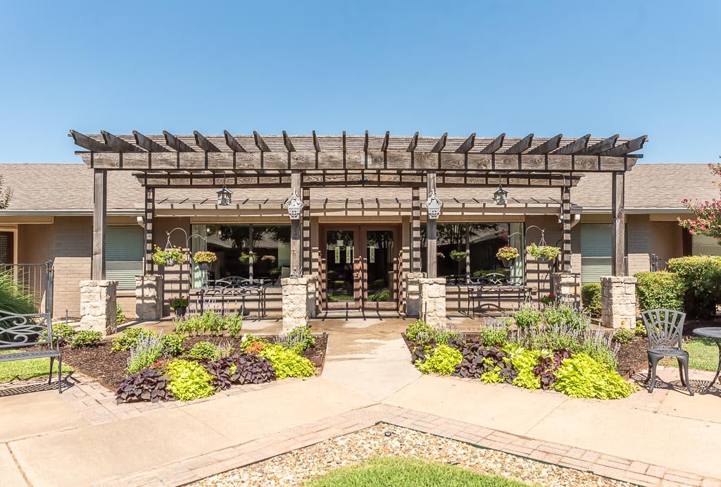 A beautifully landscaped entryway of a modern building with a pergola and garden.