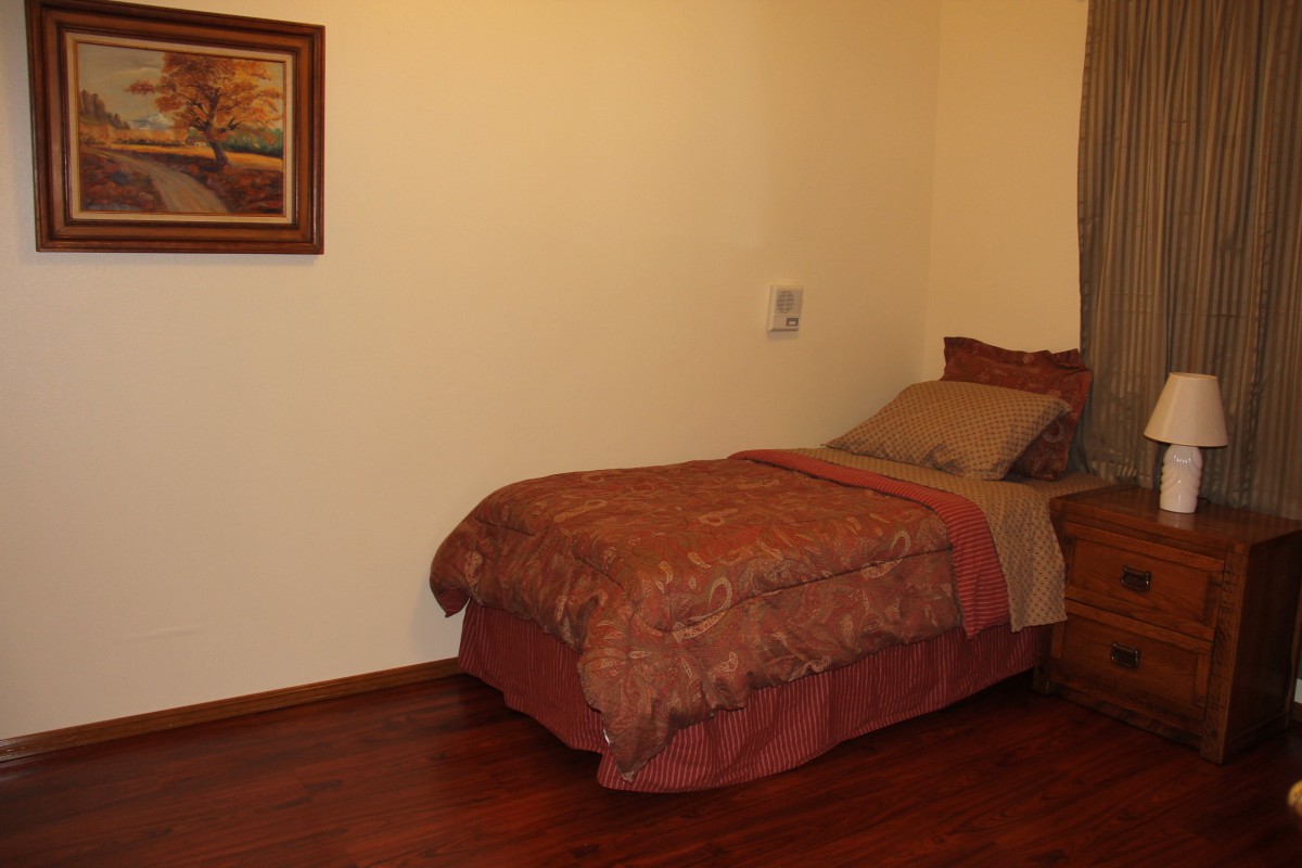 A cozy bedroom with a single bed, wooden floor, and a painting on the wall.