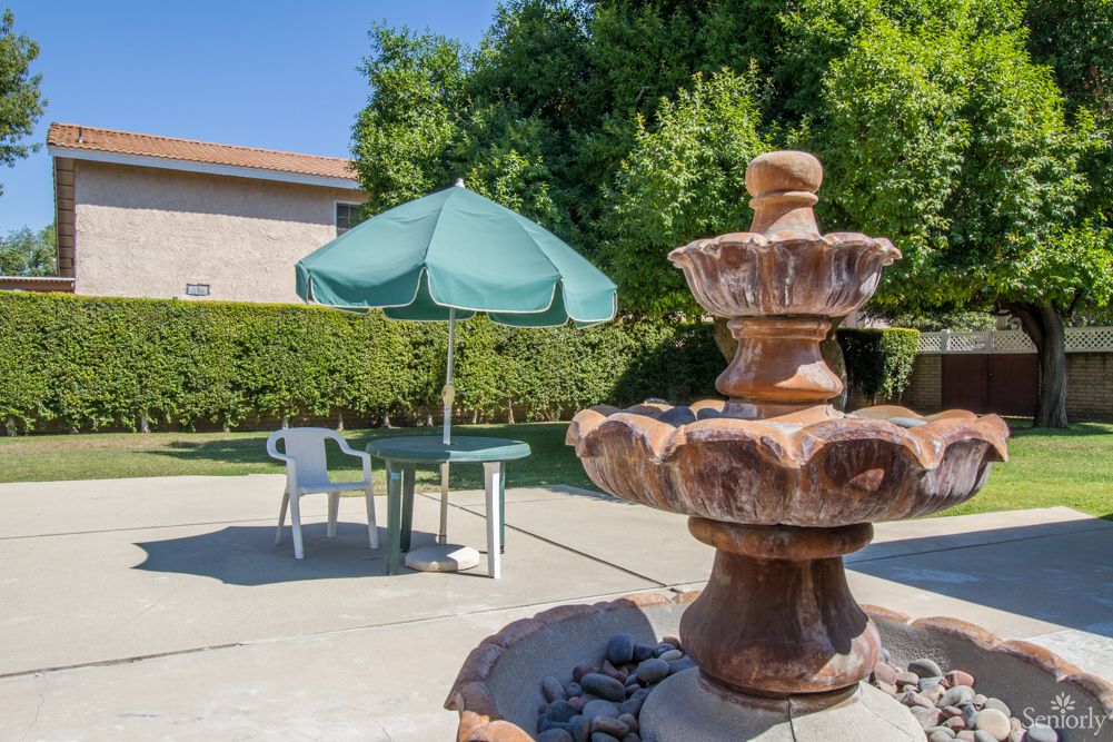 A tranquil backyard scene with a decorative fountain and a patio table shaded by an umbrella.