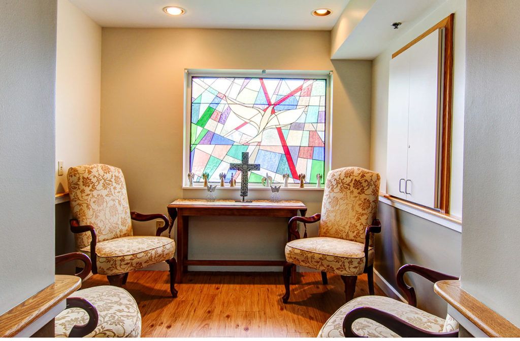 A cozy room with armchairs and a table in front of a colorful stained glass window.