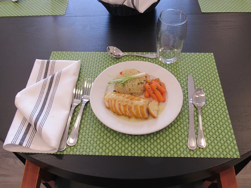 A neatly arranged table setting with a plate of food, including sliced meat and vegetables, on a green polka dot placemat.