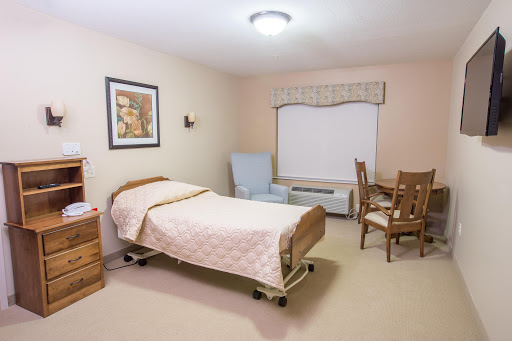 A well-lit healthcare room featuring a bed, chair, and wooden furniture that creates a comfortable atmosphere.