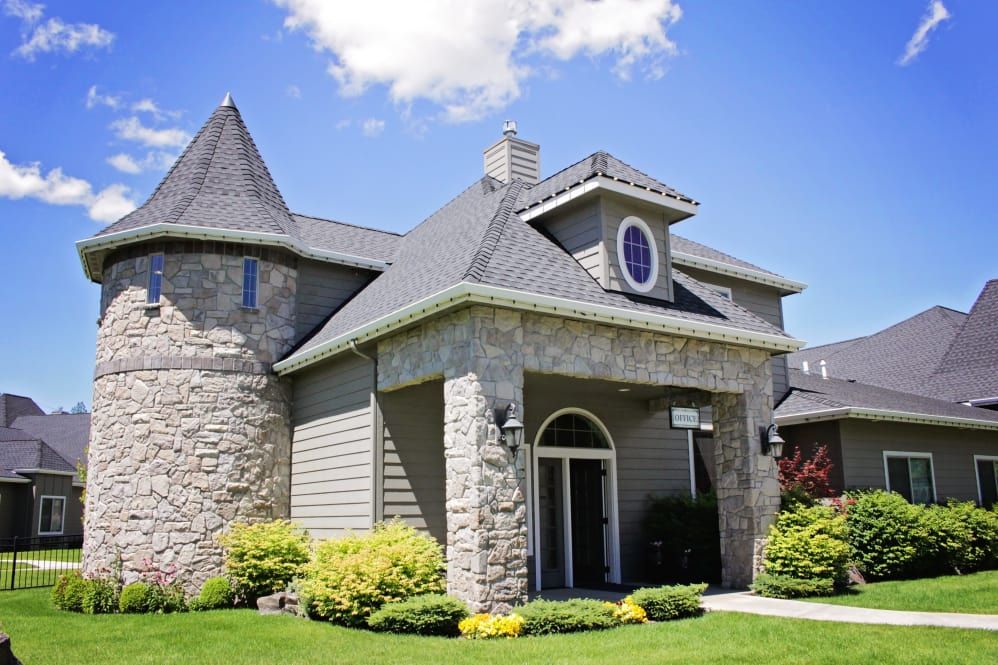 A beautiful stone house with a well-maintained lawn and landscaping under a clear blue sky.