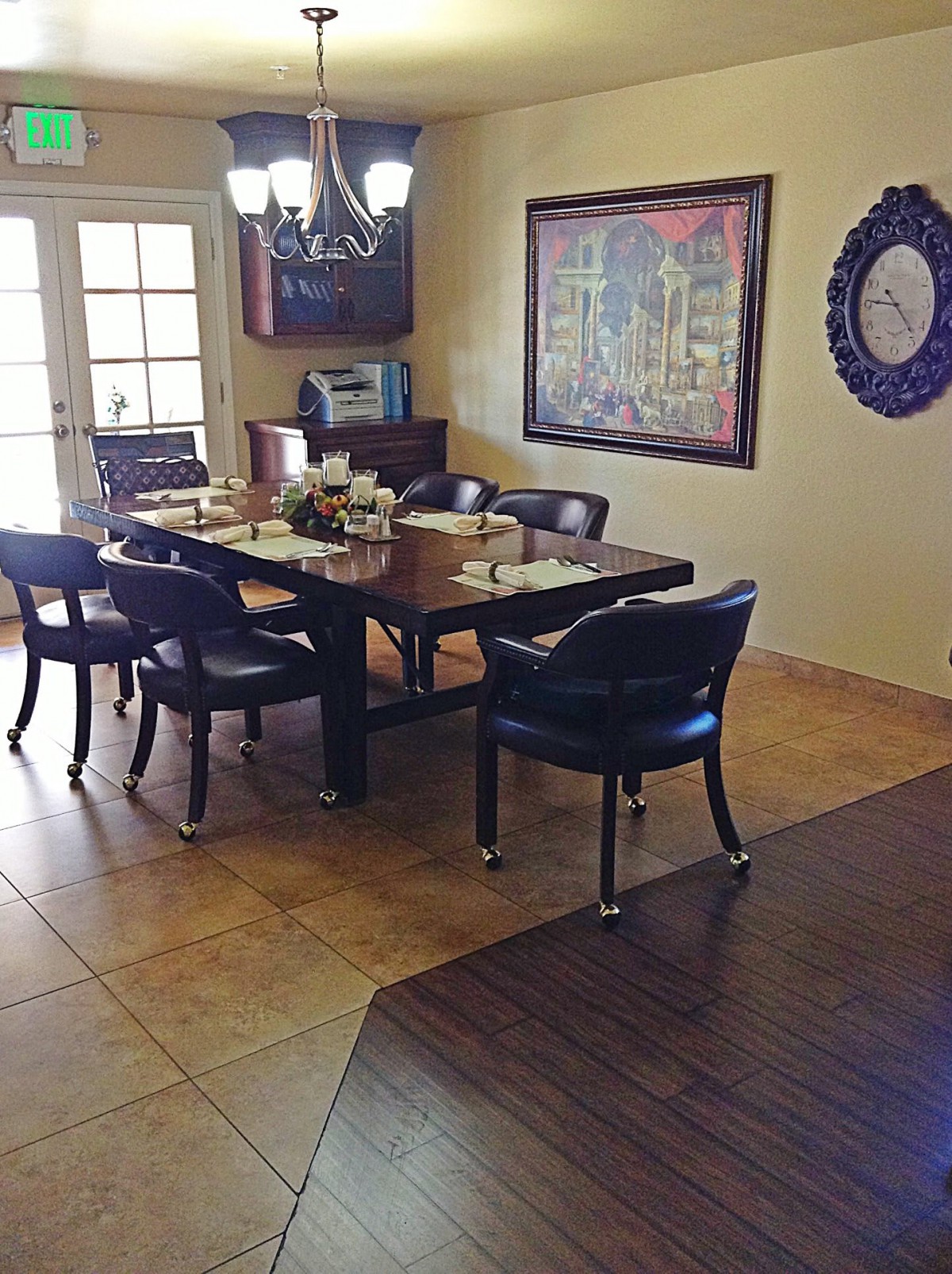 A dining room with a large table surrounded by chairs, a chandelier, and wall decor including a painting and mirror.