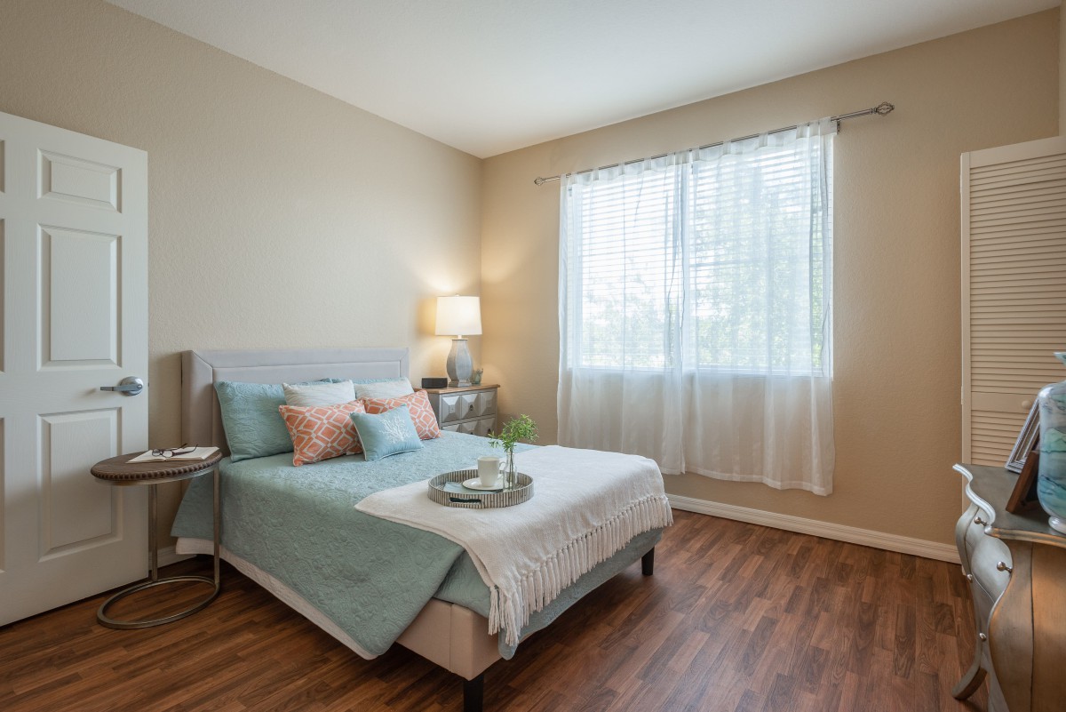A cozy bedroom with a neatly made bed, soft lighting, and a window letting in natural light.