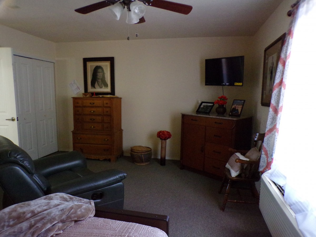 A cozy bedroom with a dresser, armchair, and television.