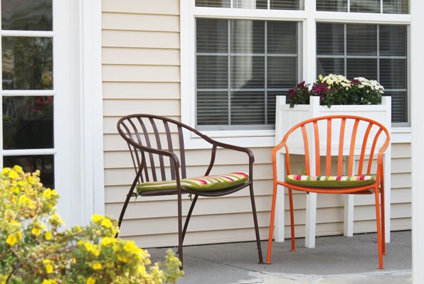 A cozy outdoor patio with two chairs, plants, and flowers by the window.