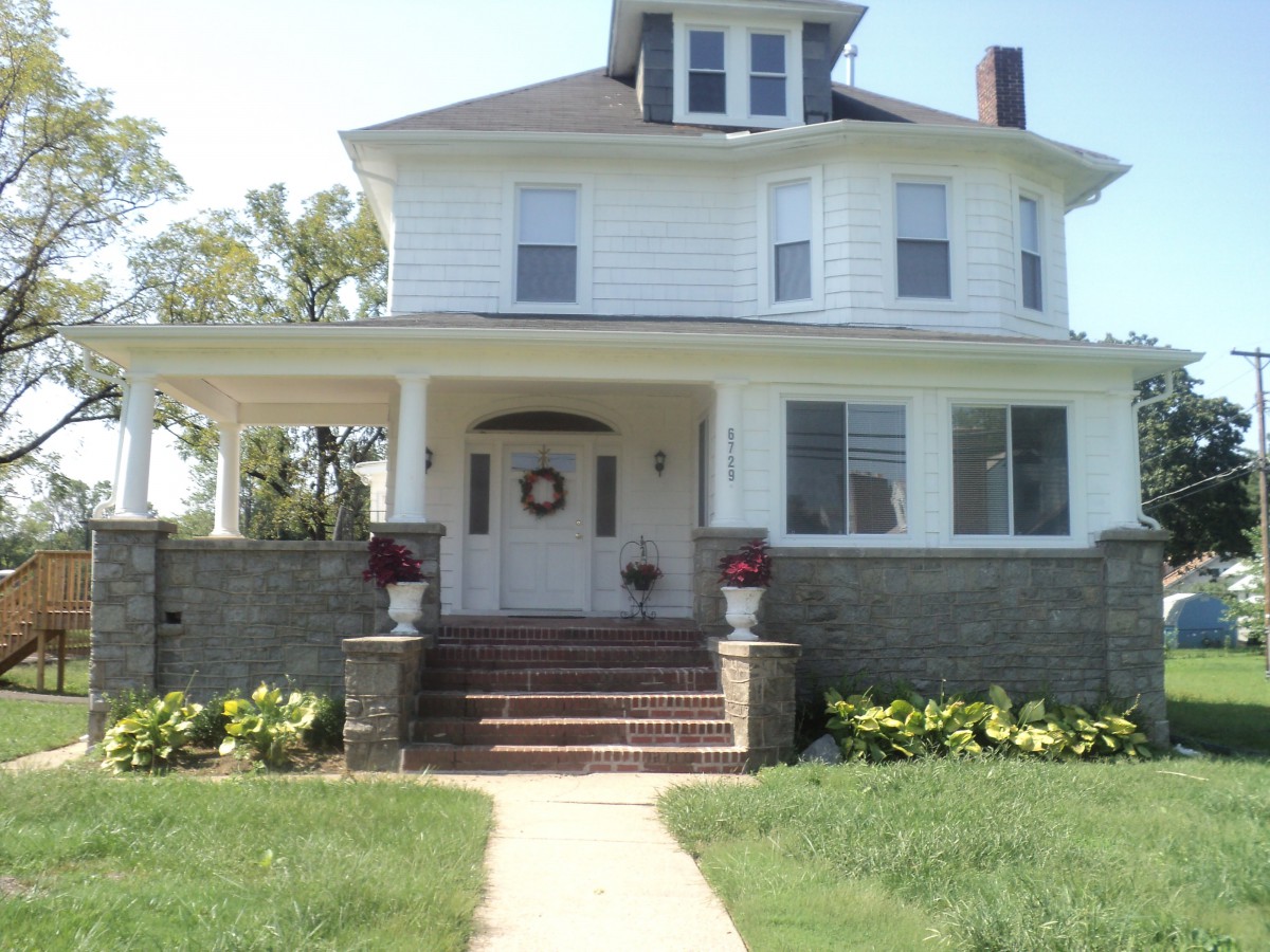 A large two-story house with a wraparound porch and a well-kept front yard.
