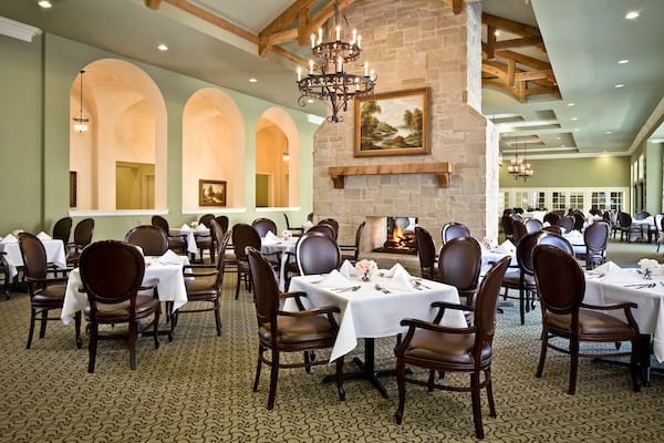 An elegantly decorated dining room with neatly arranged tables and chairs, featuring a chandelier and a warm ambiance.
