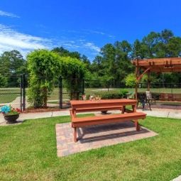A serene outdoor area featuring a picnic table and a pergola surrounded by lush greenery.