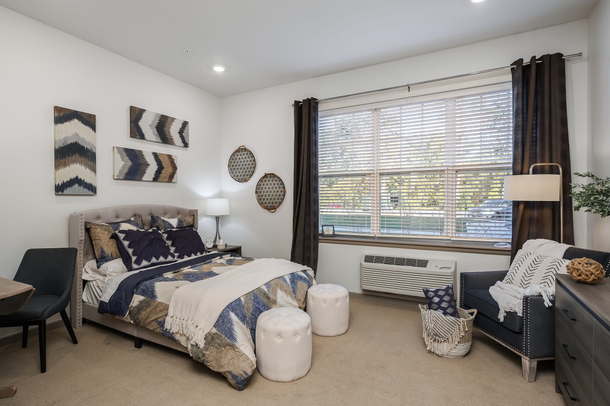 A modern bedroom featuring a well-decorated bed, ample natural light from a large window, and stylish decor elements.