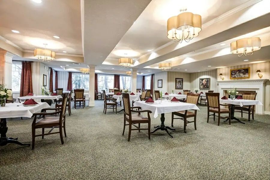 An elegantly decorated dining room with neatly arranged tables and chairs, illuminated by chandeliers.