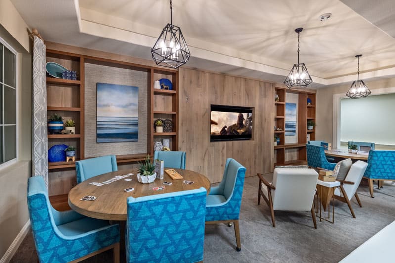 A modern dining area featuring blue upholstered chairs, wooden shelves with decorations, and soft lighting for a cozy ambiance.