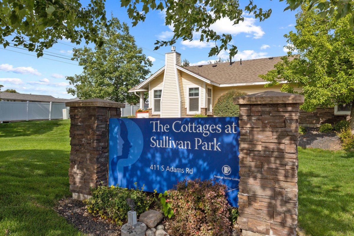A sign for 'The Cottages at Sullivan Park' in front of a residential building surrounded by trees.