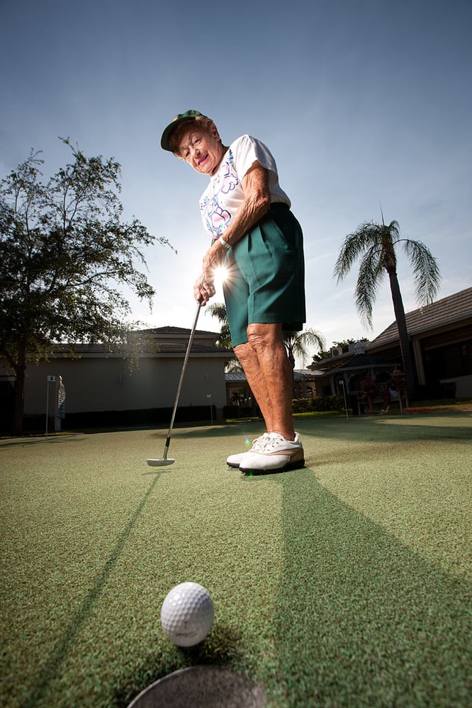 A senior person practicing putting on a golf course under clear skies.
