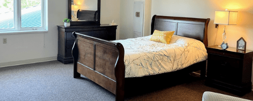 A cozy bedroom features a wooden sleigh bed and a matching dresser with a mirror.