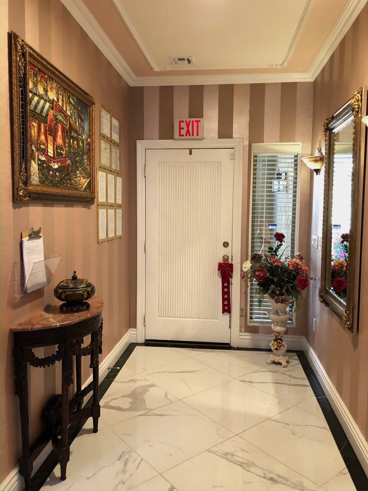 A tastefully decorated entryway featuring striped wallpaper, a large mirror, artwork, and a floral arrangement.