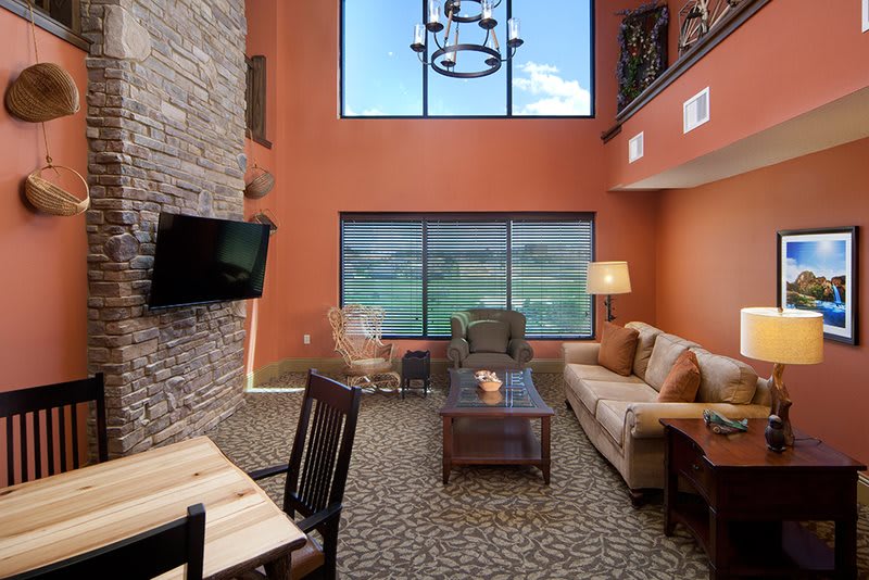 A cozy living room with high ceilings and warm decor, featuring a large window, sofa, coffee table, and wall-mounted television.