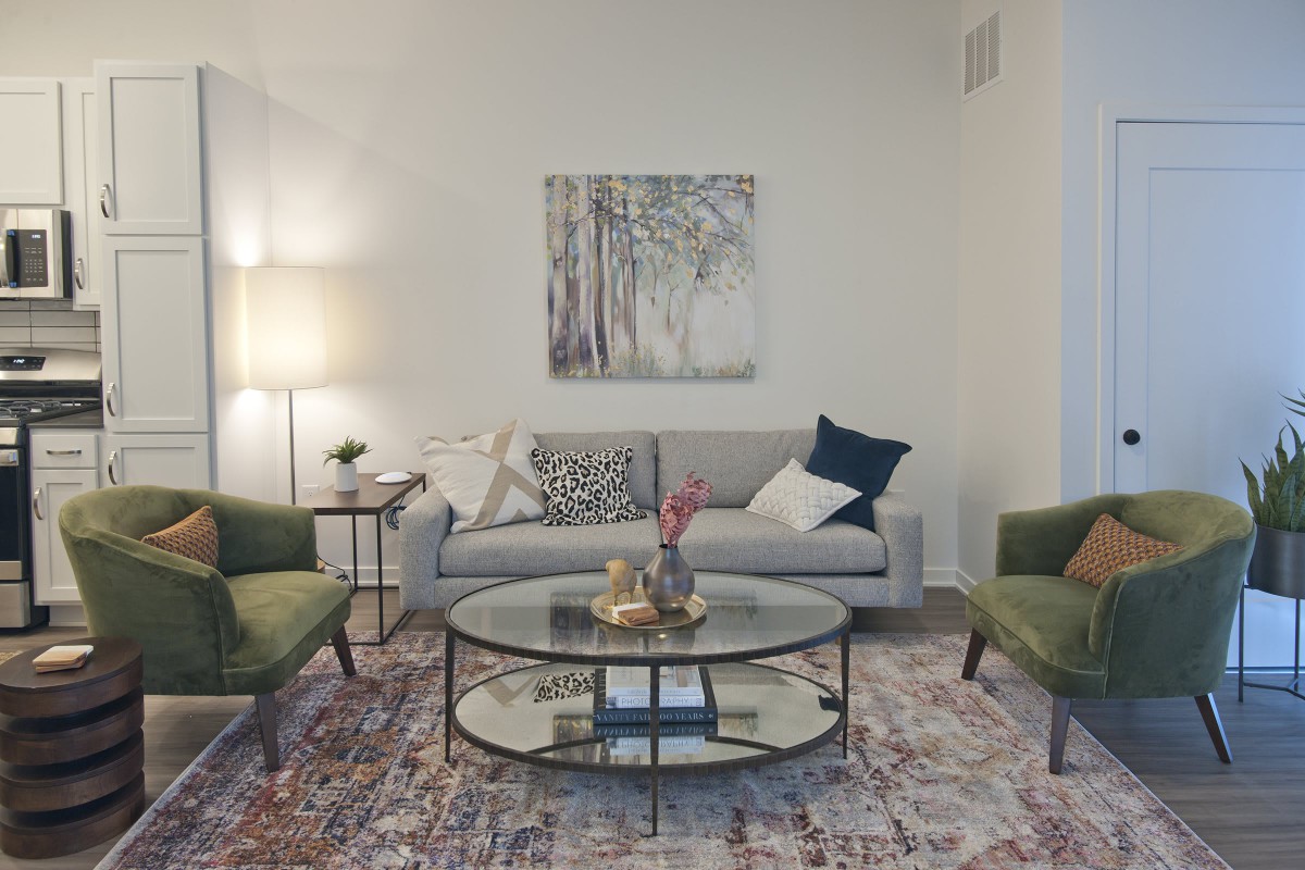 A stylish living room with a cozy sofa, two armchairs, and a glass coffee table, complemented by a decorative rug and wall art.