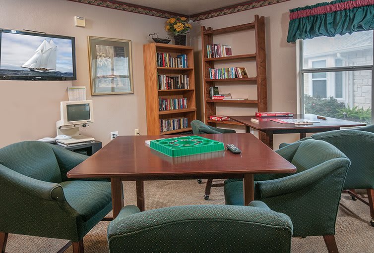 A cozy library with bookshelves, a computer, and a seating area featuring a table ready for a game.