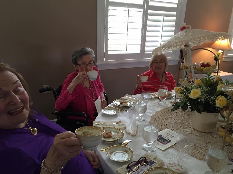 A group of elderly women enjoying a tea party with cups of tea and elegant table settings.