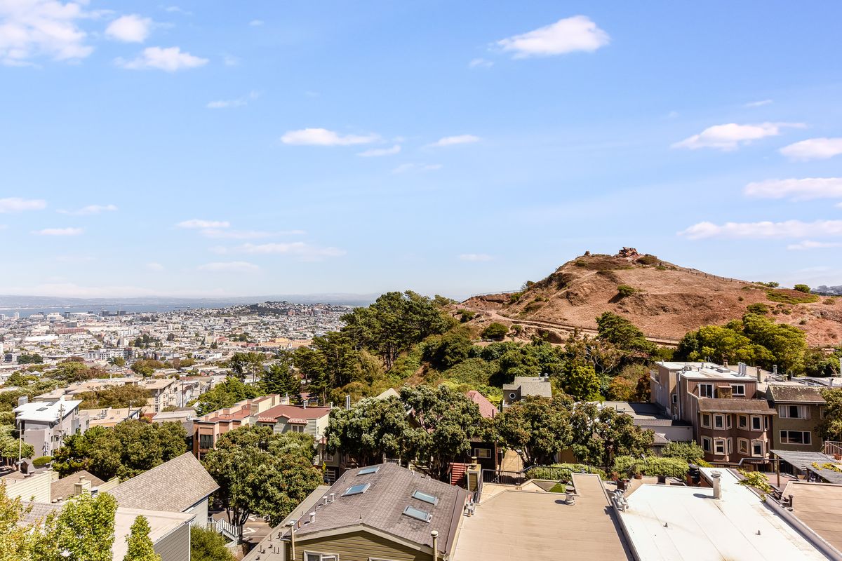 A scenic view of a hilly landscape overlooking an urban area with houses and greenery under a clear blue sky.