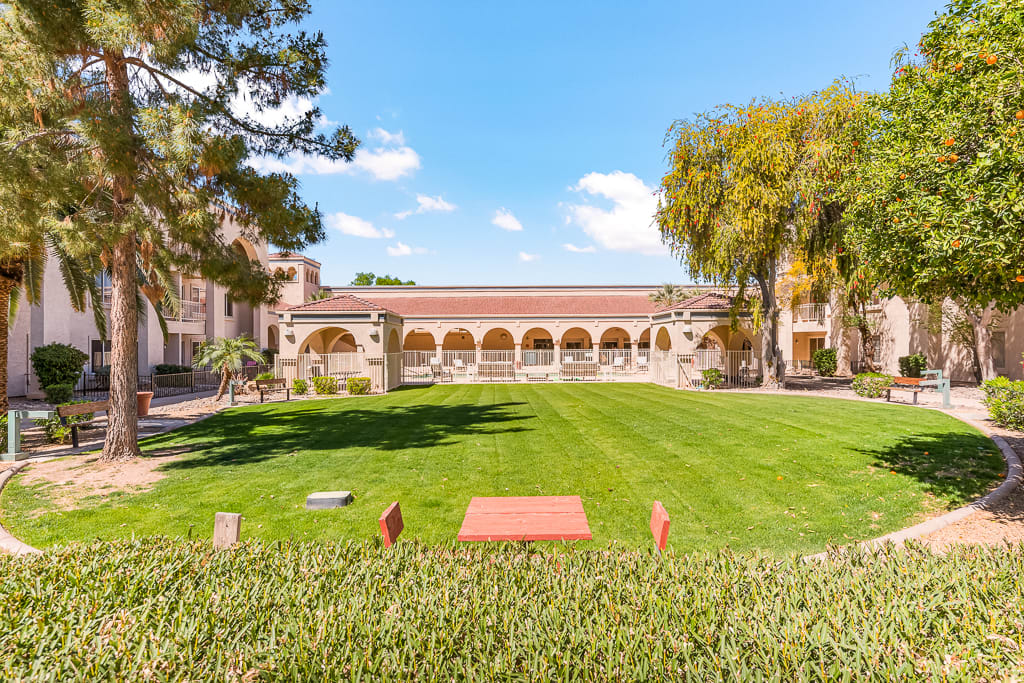 A large courtyard with a manicured lawn and arched walkways under a clear blue sky.