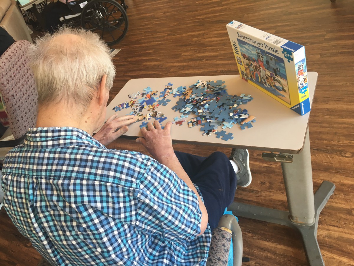 An elderly person working on a jigsaw puzzle at a table indoors.