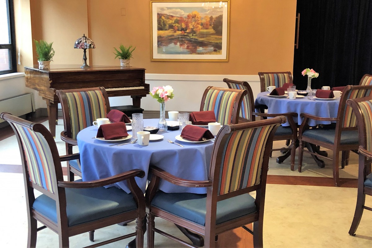 A neatly set dining area with tables and chairs, featuring a piano and artwork on the wall.