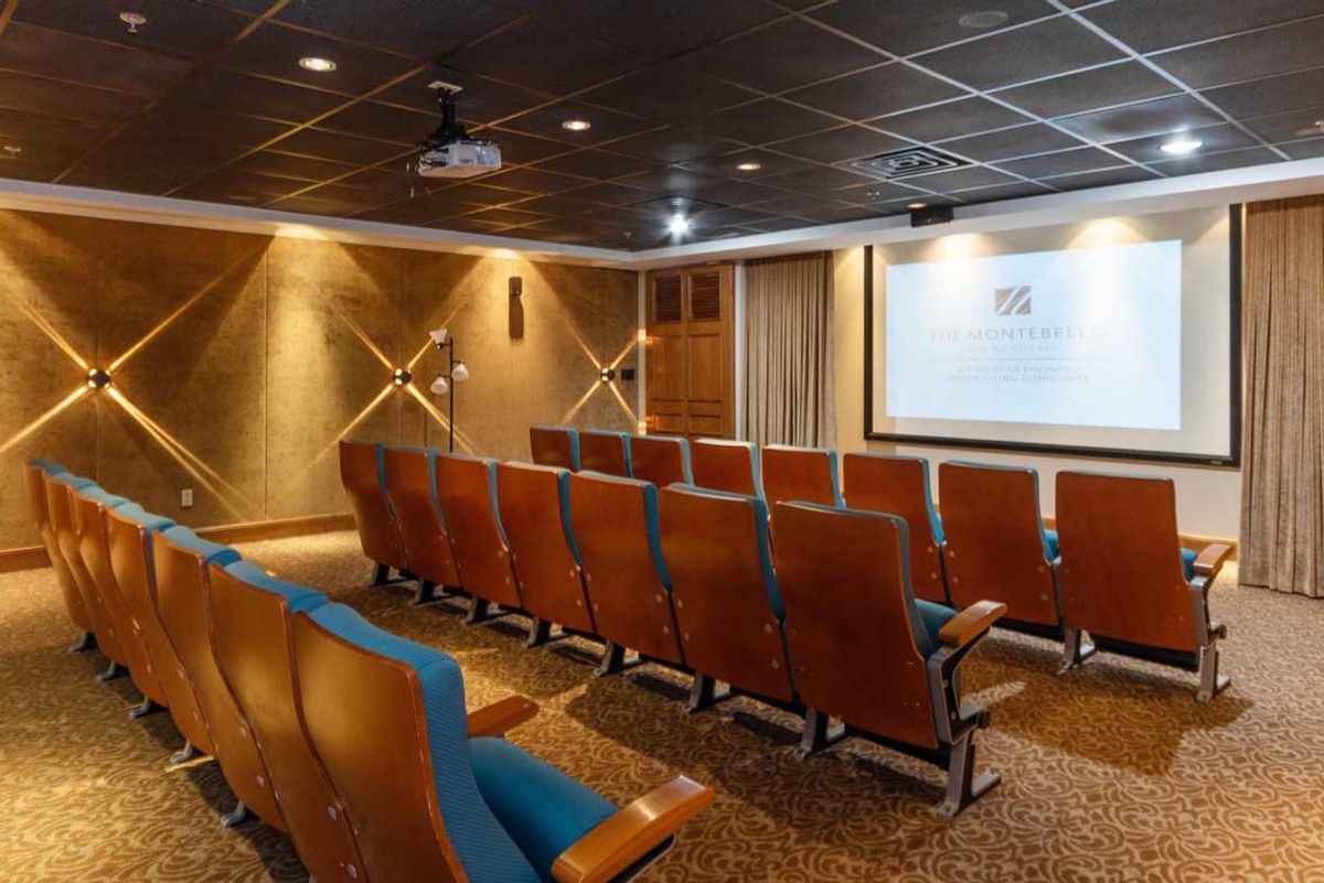 An empty theater room with rows of seats facing a projection screen.