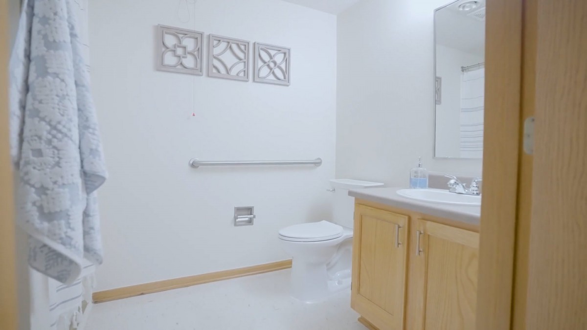 A clean and minimalist bathroom featuring a toilet, sink with a wooden cabinet, mirror, and decorative wall art.