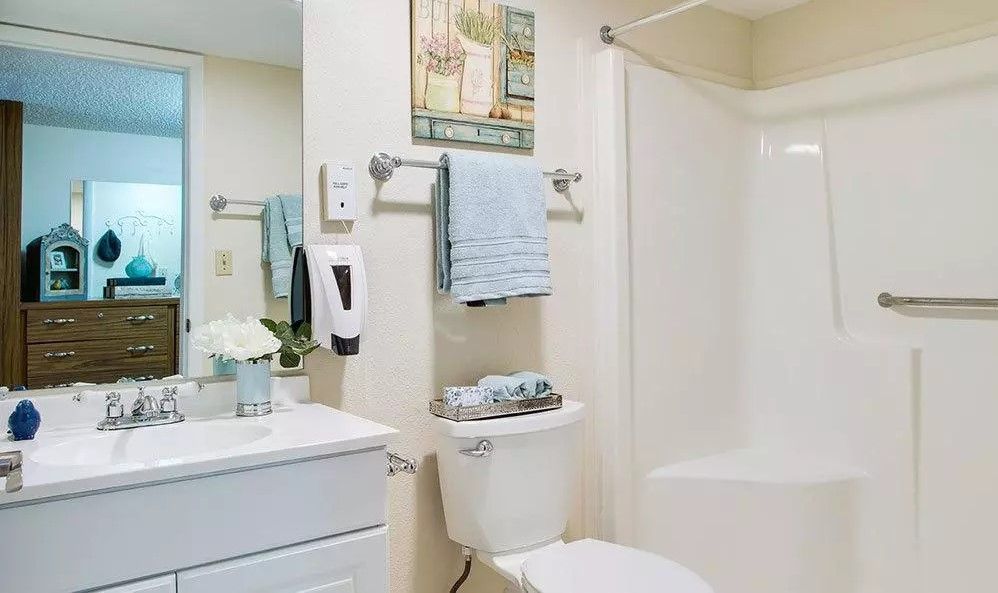 A clean and neatly organized bathroom with white fixtures, blue towels, and light decor.