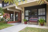 A cozy residential building with a porch, featuring a red bench and potted plants along the pathway.