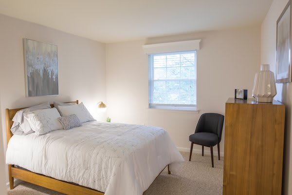 A minimalist bedroom with a neatly made double bed, a window, and a chair.