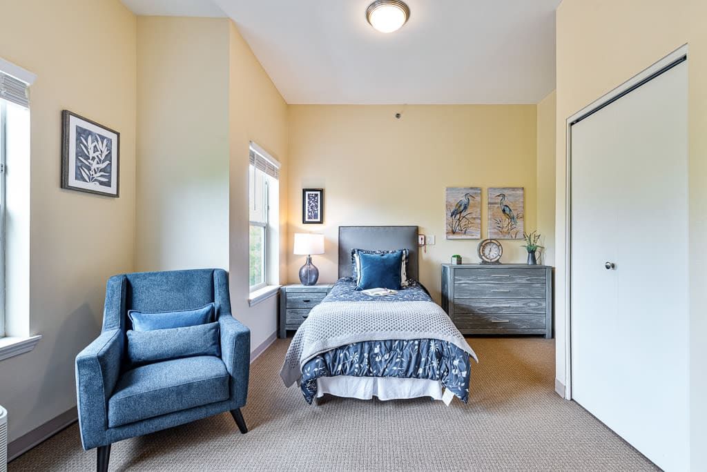 A cozy bedroom with a single bed, blue armchair, and decorative elements.