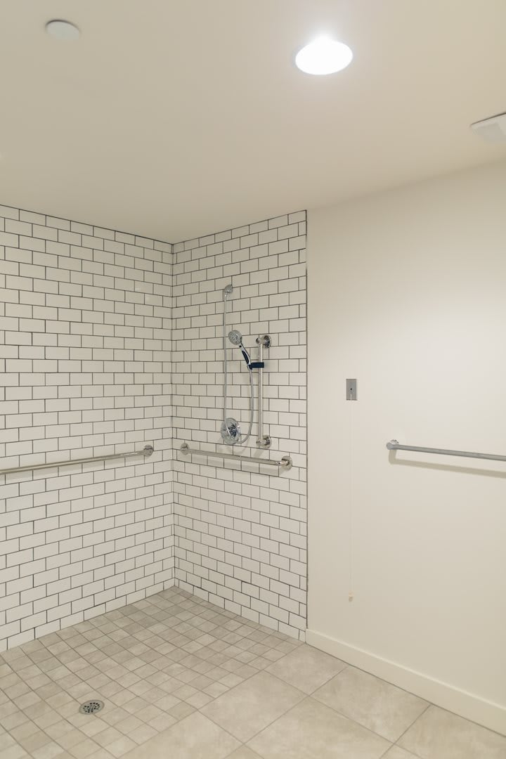 A modern minimalist bathroom with white subway tiles and handrails.