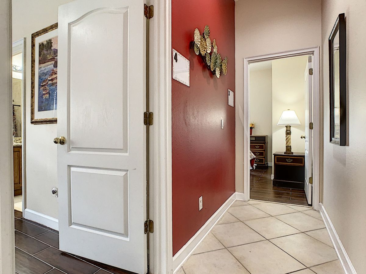 A cozy hallway with a red accent wall, white doors, and tiled flooring leading to a warmly lit room.
