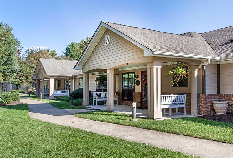 A row of small residential buildings with benches on a neatly manicured lawn under a clear blue sky.